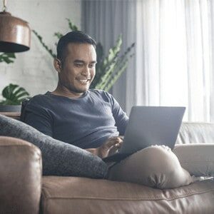 man smiling at home looking at computer sitting on the couch