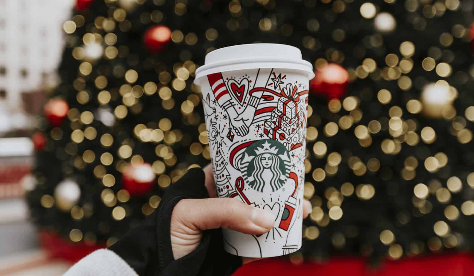 hand holding a coffee cup in front of a Christmas tree