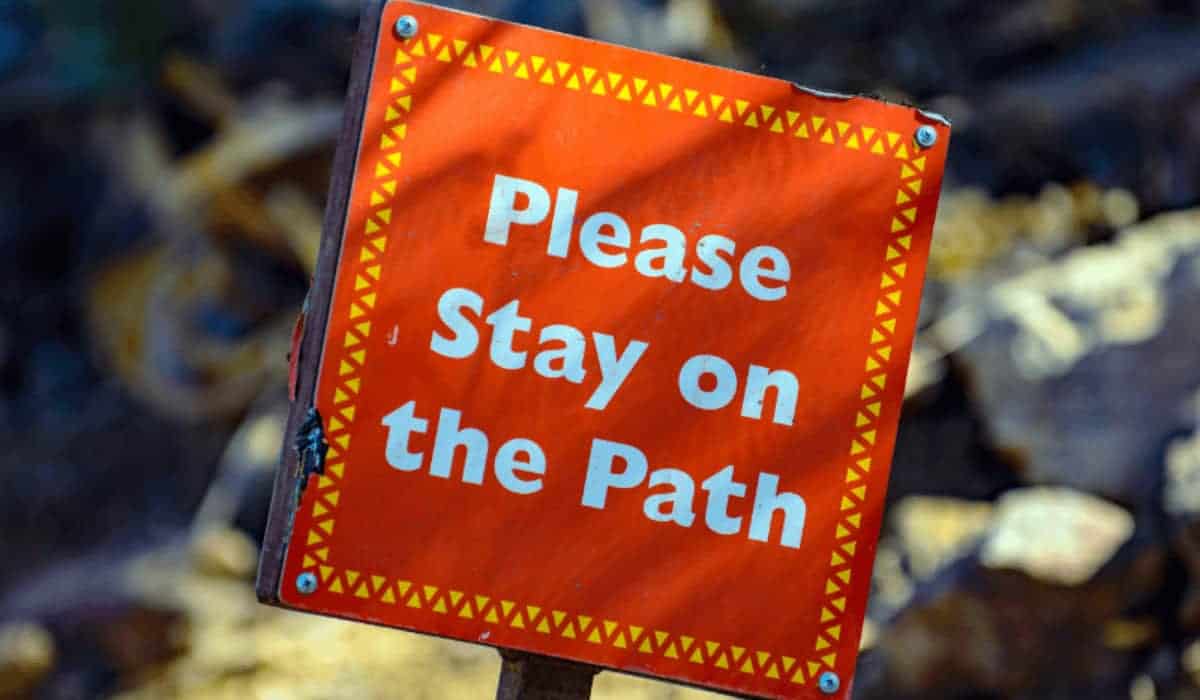 orange sign that says "please stay on the path"