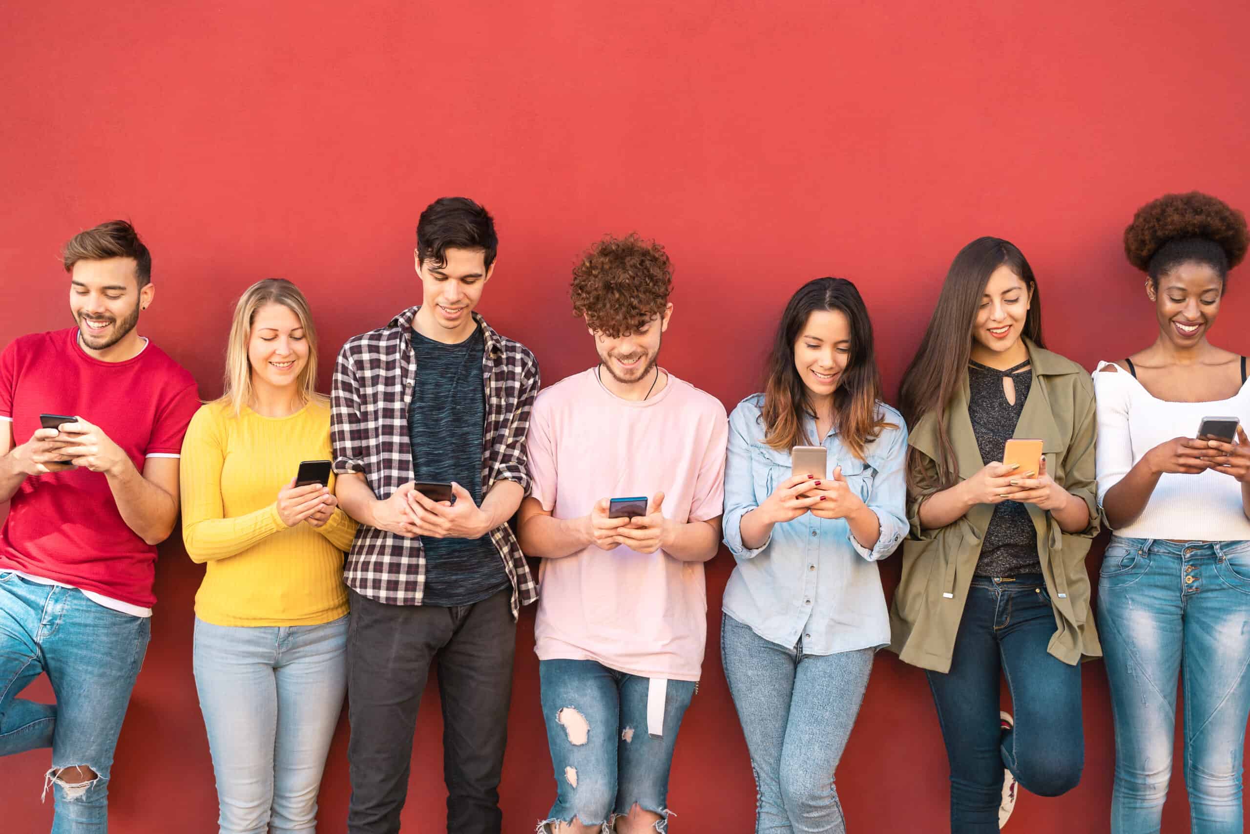 group of young adults against a red wall all on their phones
