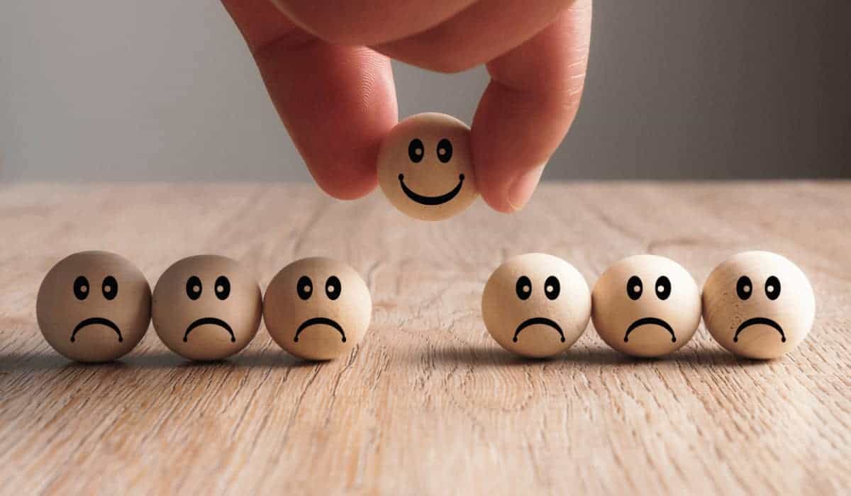 a hand picking up a wooden ball with a printed smiley face from a line of wooden balls with printed frowns