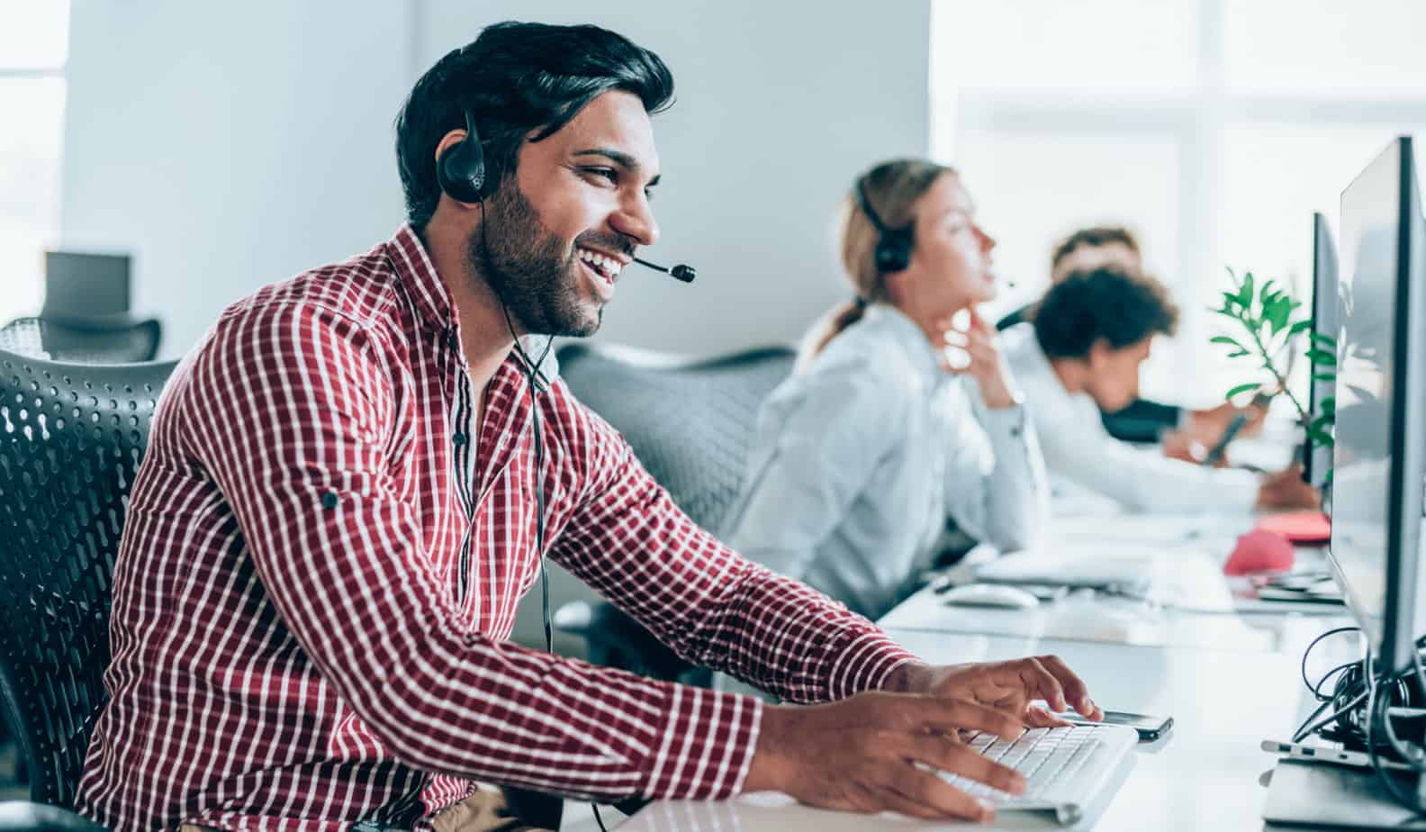 Man with headset on smiling while working on computer