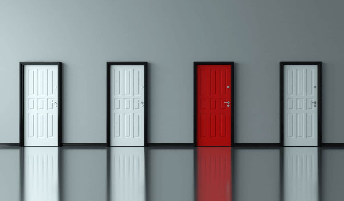 a series of four doors in a gray wall, the first, second, and fourth are white and the third is red