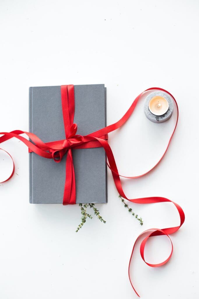 A flat lay image of a box being wrapped in red ribbon.