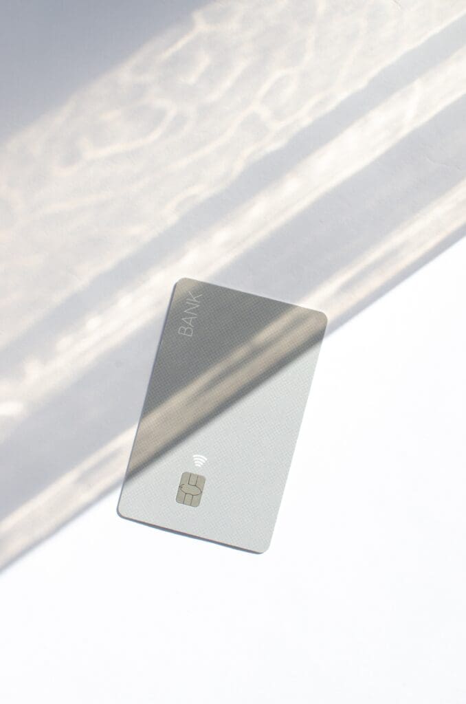 A gray credit card laying on a white surface with shadows falling across