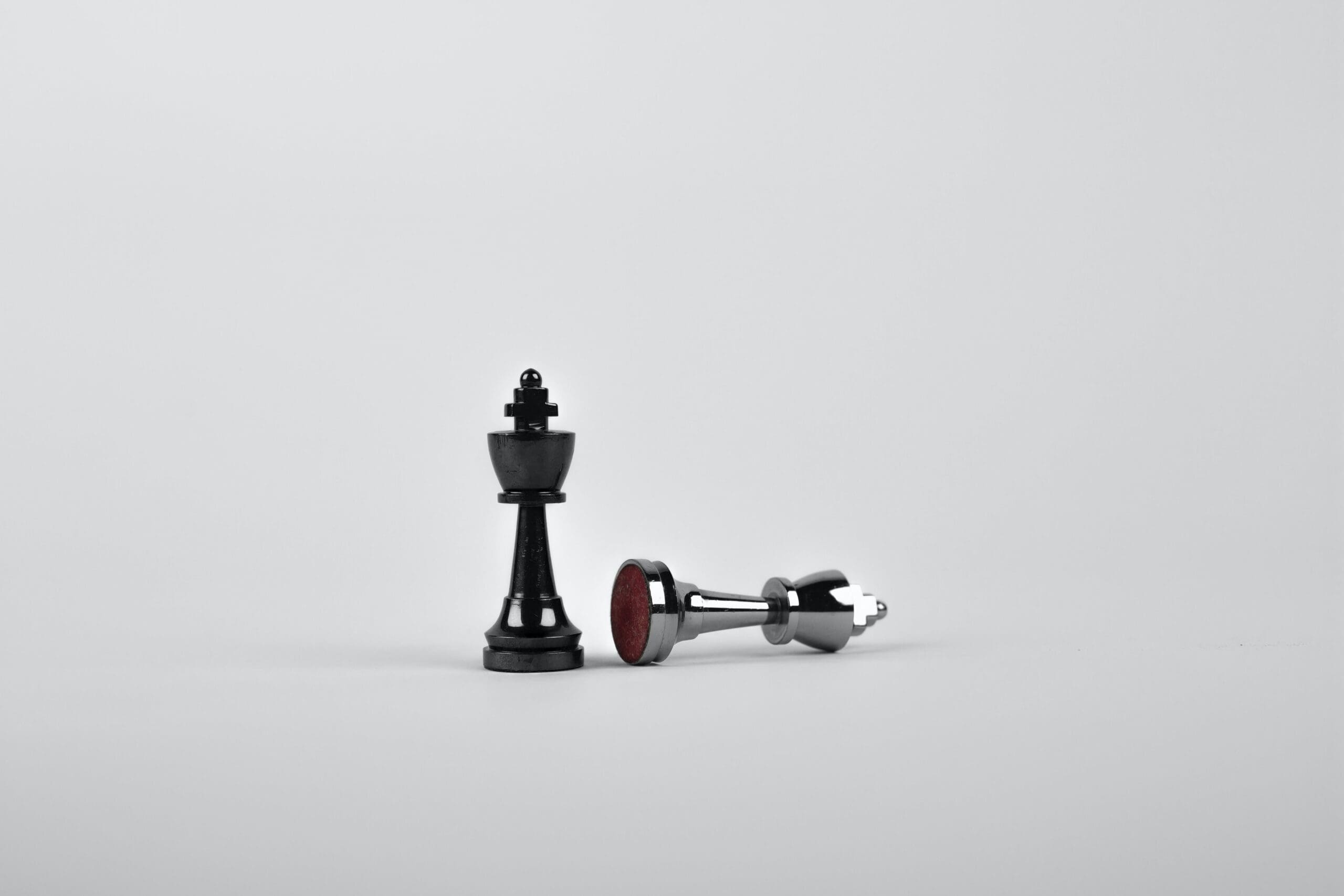 A black king chess piece next to a toppled silver chess piece